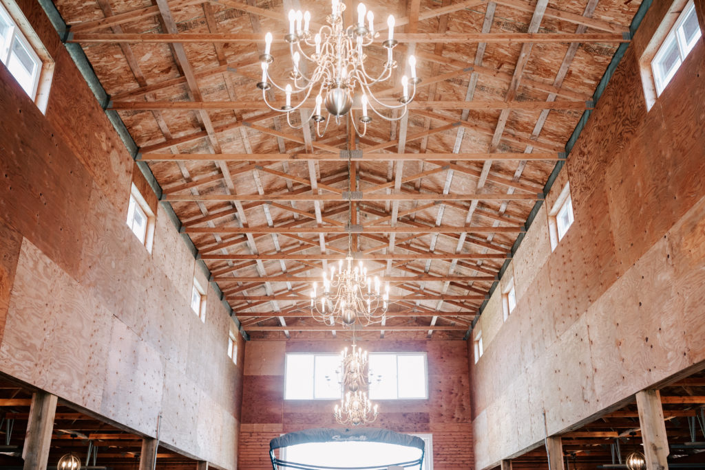 Four illuminated chandeliers hanging through the beams of the rustic country barn