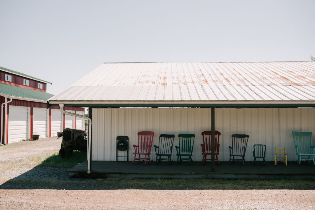A variety of chairs propped in the shade near the big red barn, with a view of wraparound white garage doors