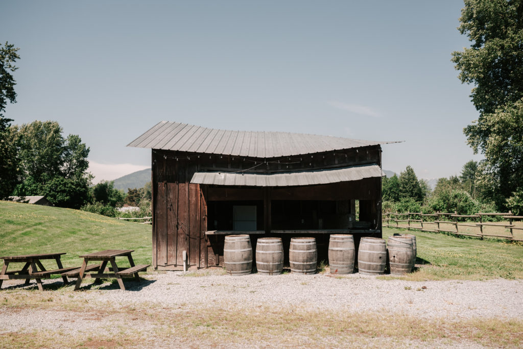 The rustic wooden outdoor bar with big barrels and picnic tables with grassy fields in the background