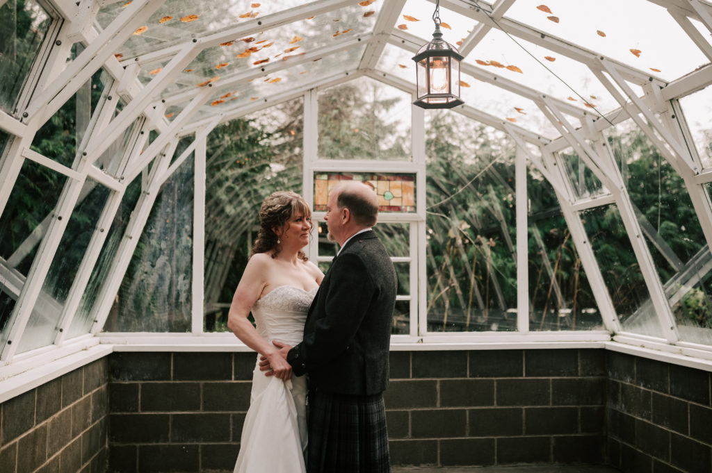A bride and groom dance underneath a lantern and glass pane dome ceiling in a small Greenhouse
